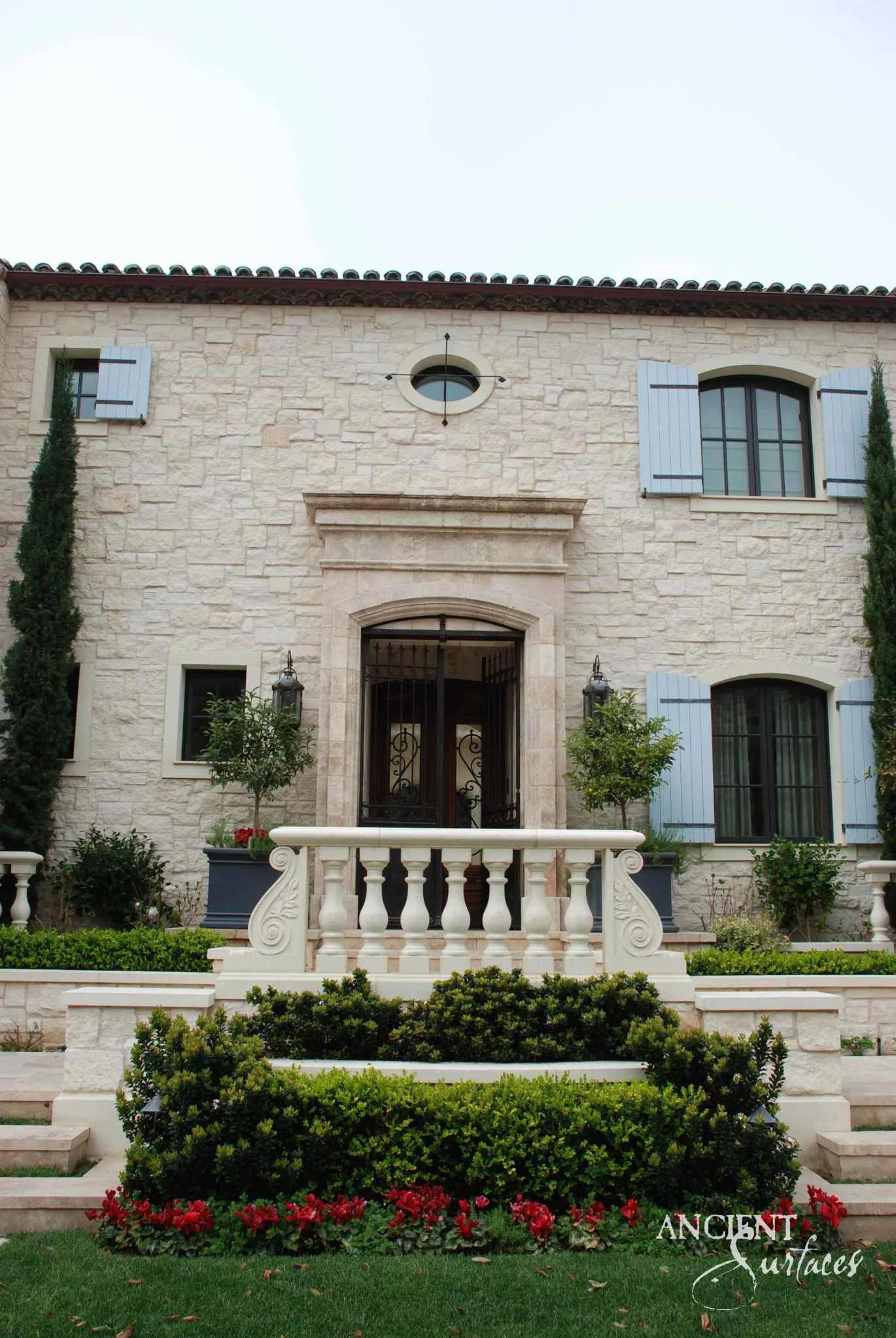 Raised arched limestone entry behind a carved stone balustrade on a French-country façade