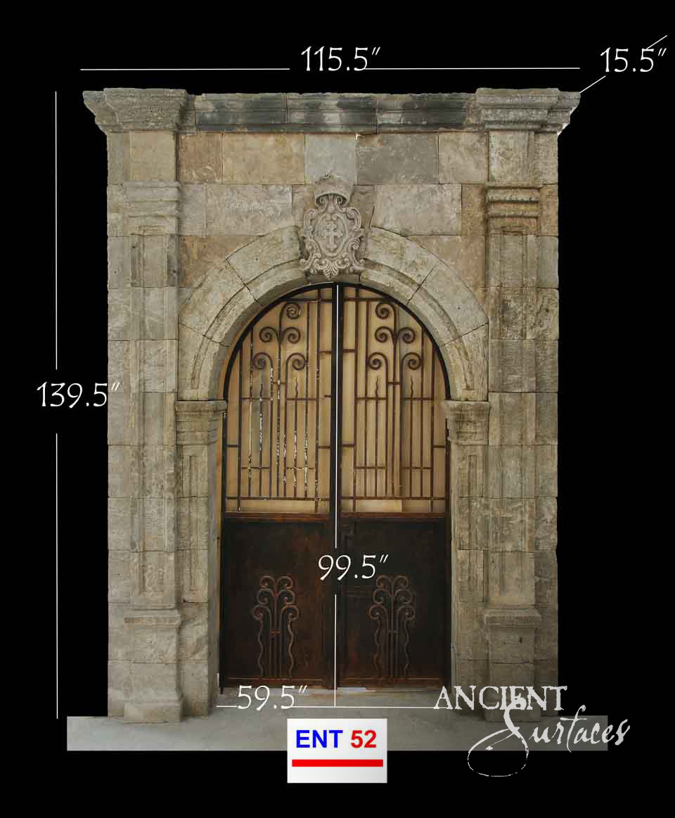 Tall carved limestone entrance surround with a round arch, cartouche crest and iron-and-wood doors