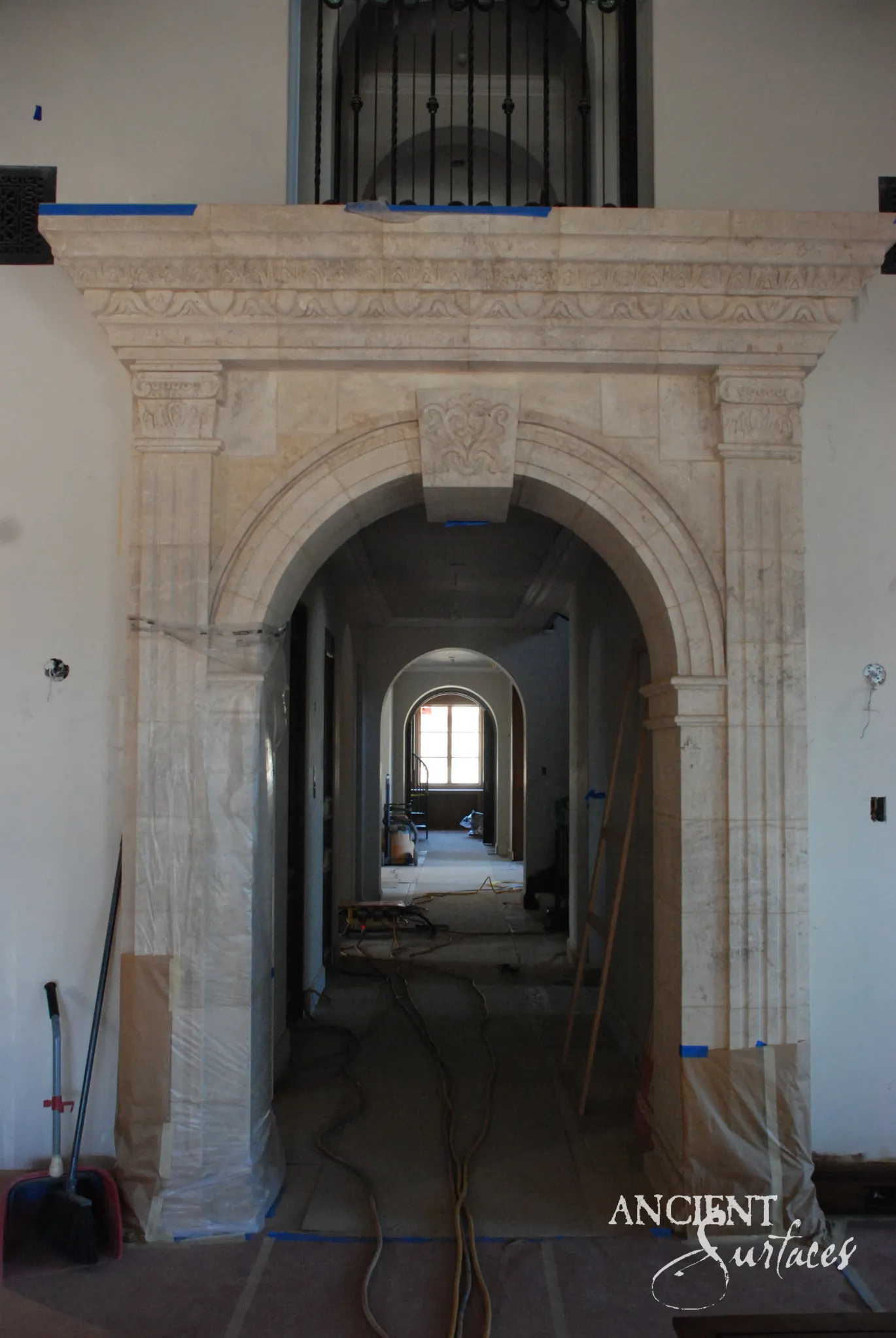 Cream limestone interior arch with carved frieze and fluted pilasters framing a hallway