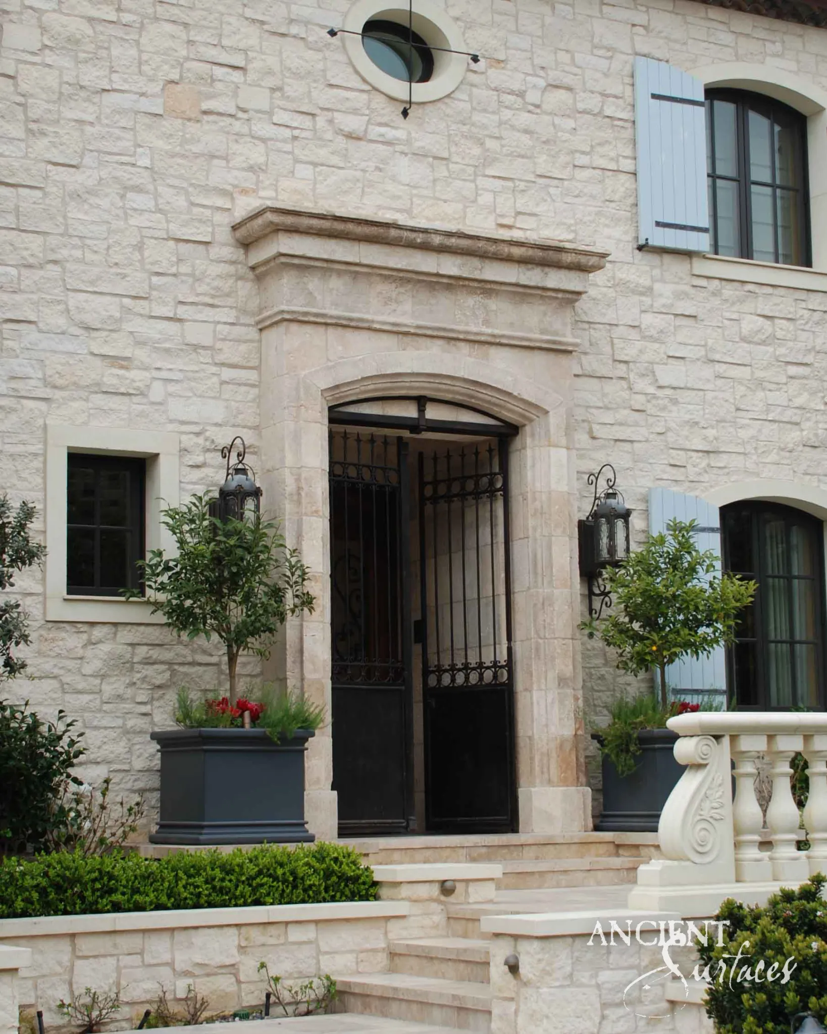 Reclaimed antique limestone entryway with an iron gate flanked by potted citrus trees